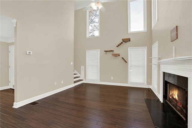 unfurnished living room with a high ceiling, dark wood-type flooring, ceiling fan, and crown molding