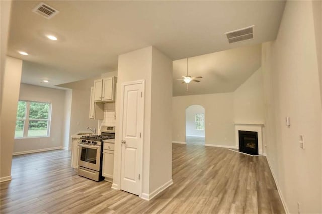 960 Park Place St, Social Circle, GA 30025 - kitchen with stainless steel gas range oven, a ceiling fan, light wood-style flooring, arched walkways, and a fireplace