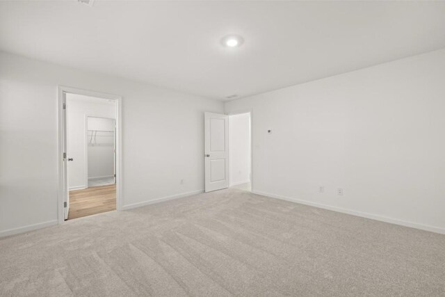 unfurnished bedroom with light colored carpet, a walk in closet, and a closet