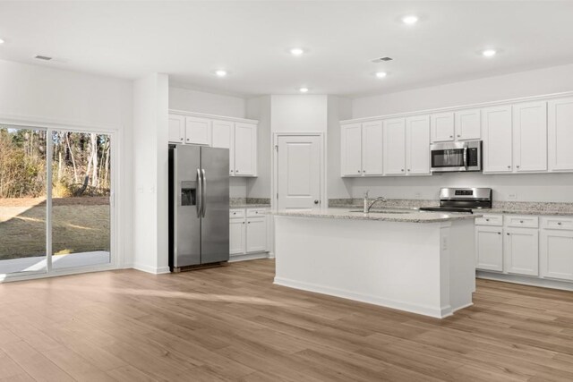 kitchen featuring white cabinets, a center island with sink, light wood-type flooring, light stone counters, and stainless steel appliances