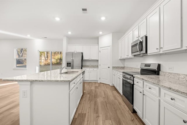 kitchen with light hardwood / wood-style flooring, an island with sink, appliances with stainless steel finishes, light stone counters, and white cabinetry