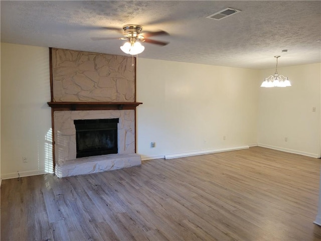 unfurnished living room featuring hardwood / wood-style flooring, ceiling fan with notable chandelier, a stone fireplace, and a textured ceiling