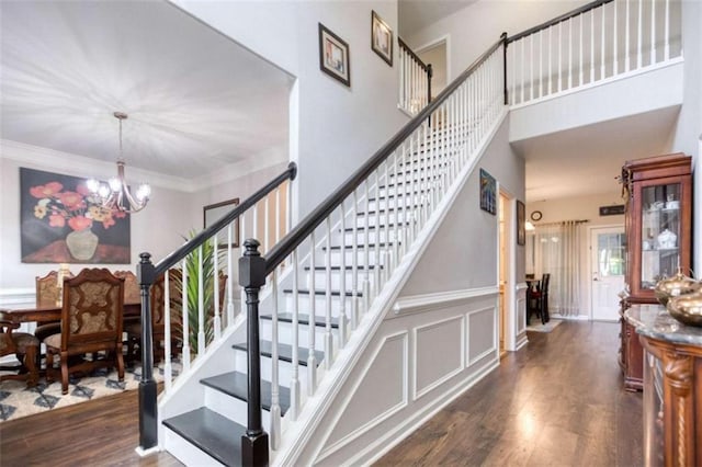 stairs with a chandelier, wood finished floors, and crown molding