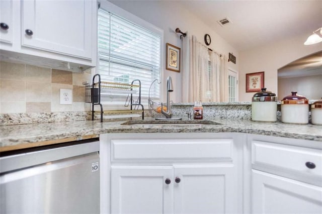kitchen featuring stainless steel dishwasher, a sink, decorative backsplash, white cabinets, and arched walkways