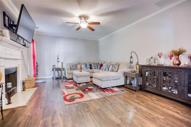 living area with ceiling fan, wood finished floors, ornamental molding, a fireplace with raised hearth, and baseboards