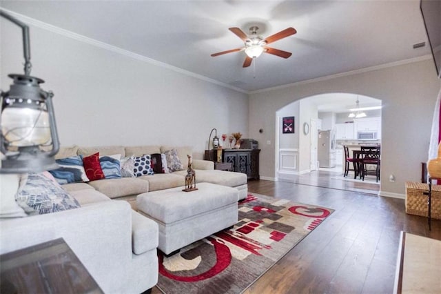 living room featuring arched walkways, a ceiling fan, wood-type flooring, ornamental molding, and baseboards