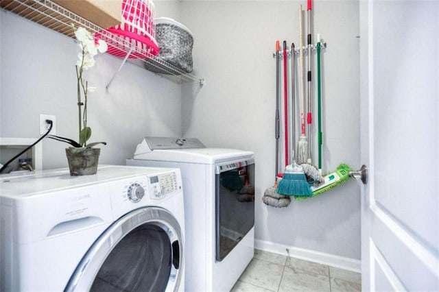 clothes washing area with washer and clothes dryer, baseboards, and light tile patterned floors