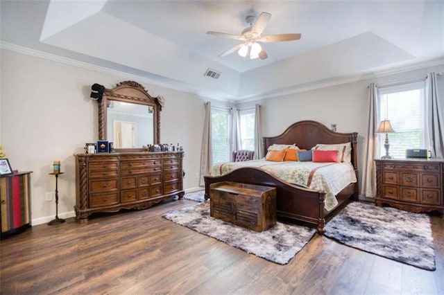bedroom with a tray ceiling, wood finished floors, multiple windows, baseboards, and ornamental molding