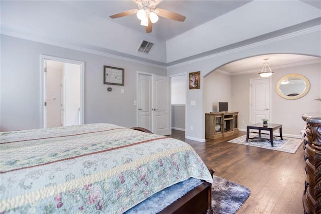 bedroom with arched walkways, dark wood finished floors, a tray ceiling, crown molding, and baseboards