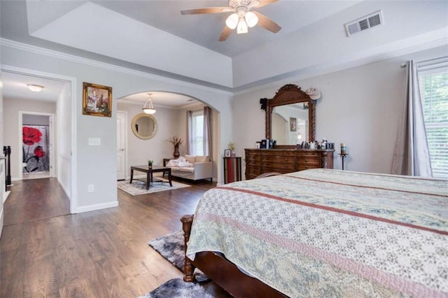 bedroom featuring arched walkways, multiple windows, wood finished floors, crown molding, and baseboards