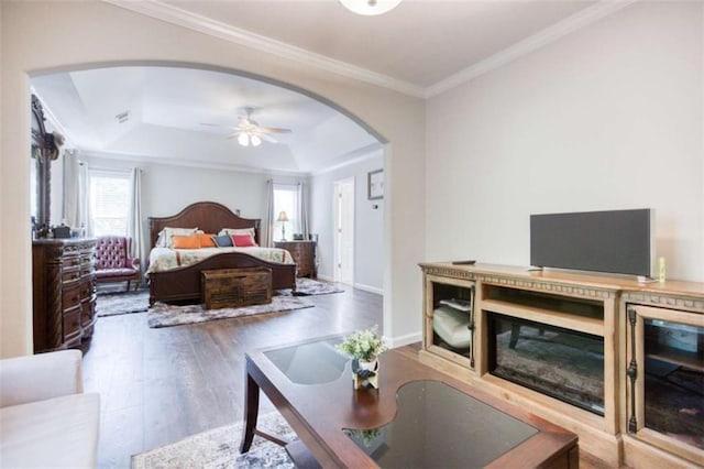bedroom featuring arched walkways, a tray ceiling, wood finished floors, ornamental molding, and beverage cooler