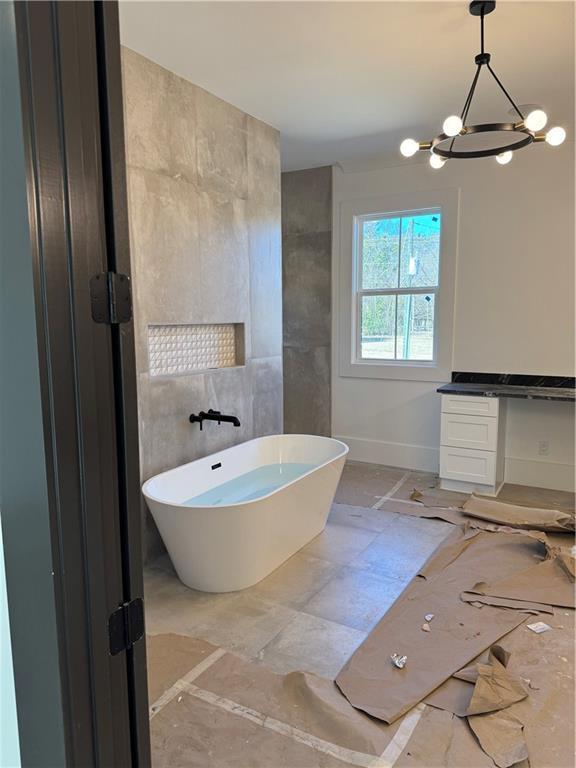 bathroom featuring a soaking tub, a notable chandelier, vanity, and baseboards