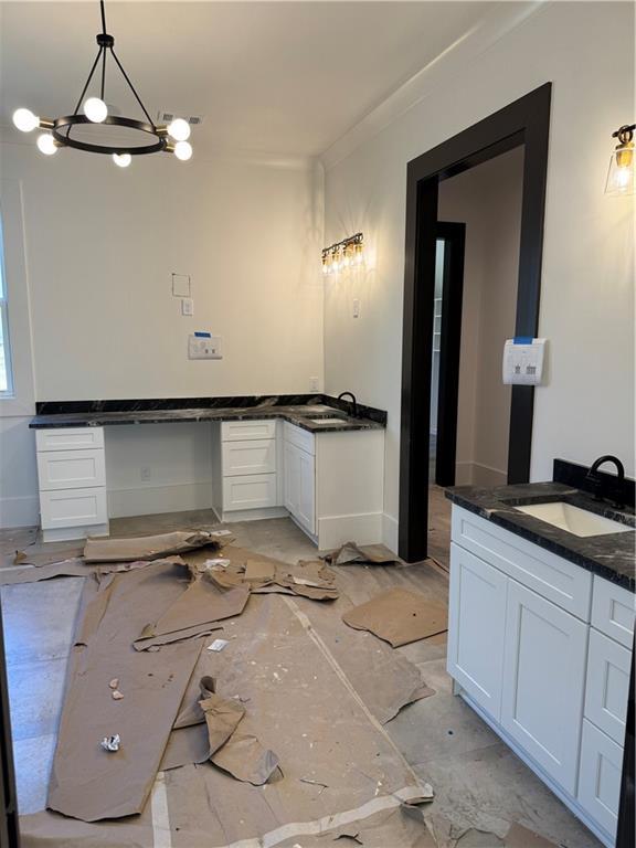 bathroom featuring a notable chandelier, baseboards, two vanities, and a sink