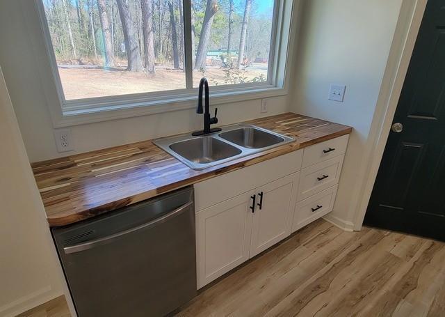 kitchen featuring black dishwasher, light wood-style floors, white cabinetry, a sink, and wood counters