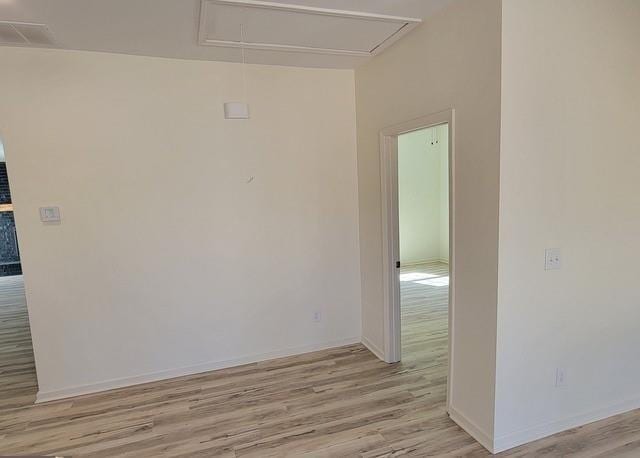 empty room with attic access, light wood-style flooring, and baseboards