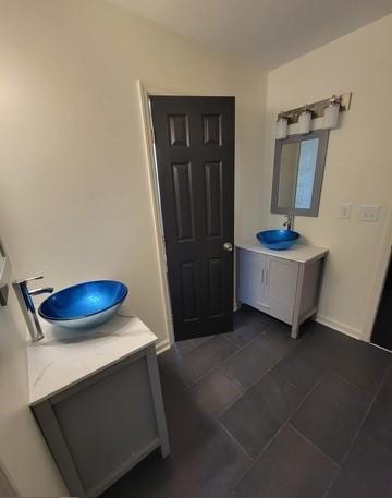 full bath with a sink, two vanities, and baseboards