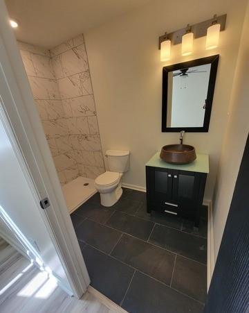 bathroom with baseboards, a tile shower, vanity, and toilet