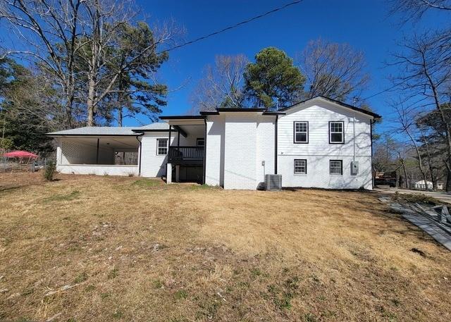 back of house featuring central AC, brick siding, and a lawn