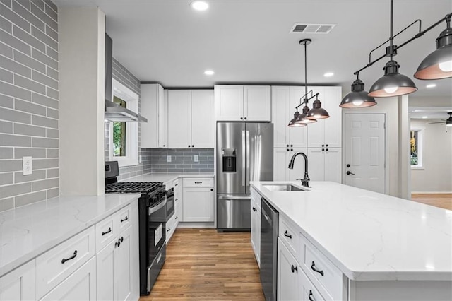 kitchen featuring decorative backsplash, appliances with stainless steel finishes, a kitchen island with sink, sink, and white cabinetry