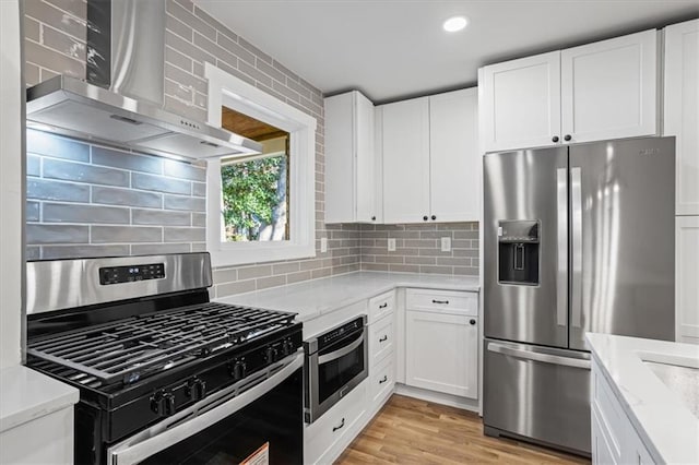 kitchen with wall chimney exhaust hood, light stone counters, light hardwood / wood-style floors, white cabinets, and appliances with stainless steel finishes