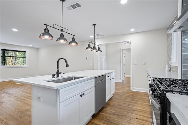 kitchen with pendant lighting, a kitchen island with sink, white cabinets, sink, and stainless steel appliances