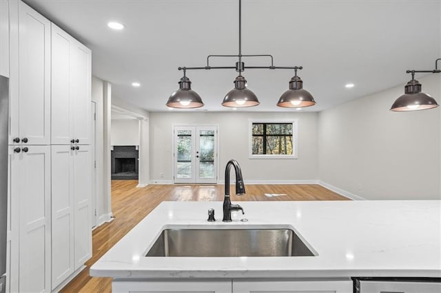 kitchen featuring french doors, white cabinets, sink, hanging light fixtures, and light hardwood / wood-style flooring