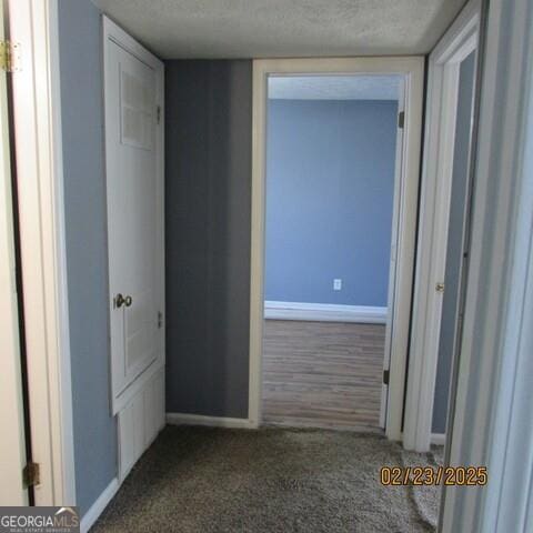 hall featuring a textured ceiling, baseboards, and dark colored carpet