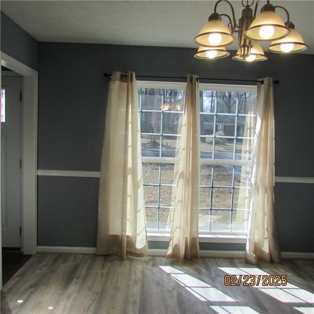 unfurnished dining area featuring a chandelier, baseboards, and wood finished floors