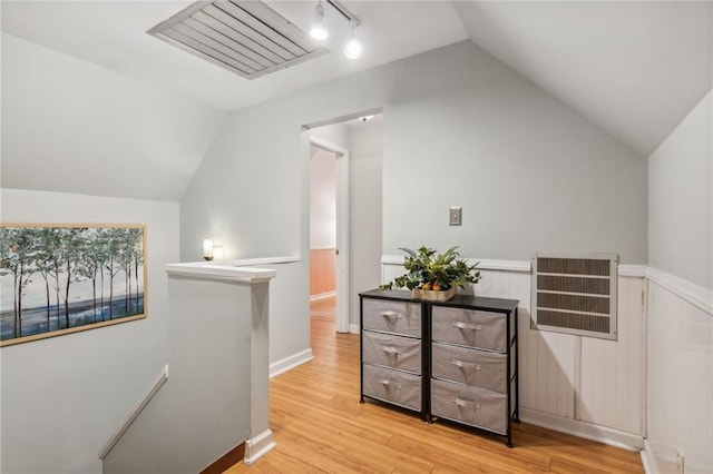 hall featuring visible vents, a wainscoted wall, vaulted ceiling, an upstairs landing, and light wood-type flooring