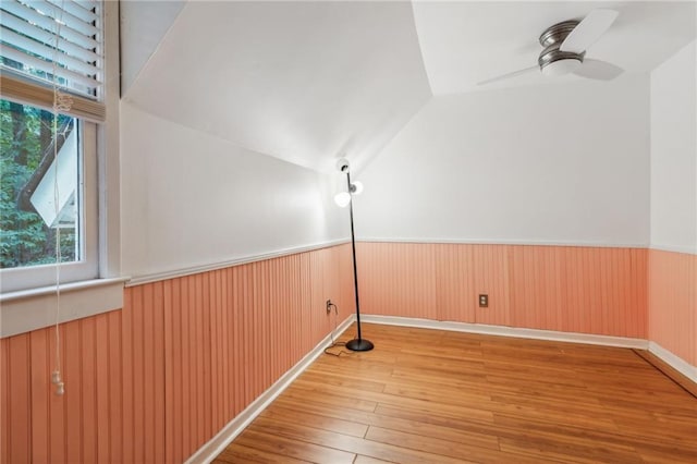 interior space with light wood-type flooring, a wainscoted wall, vaulted ceiling, and a ceiling fan