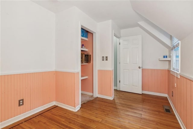 bonus room with a wainscoted wall, visible vents, wood finished floors, and wood walls