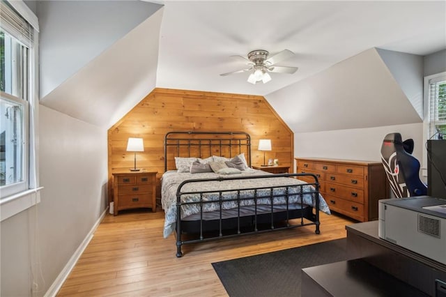 bedroom with light wood finished floors, baseboards, ceiling fan, vaulted ceiling, and wood walls