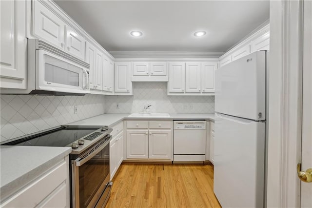 kitchen with white appliances, sink, backsplash, white cabinetry, and light hardwood / wood-style floors