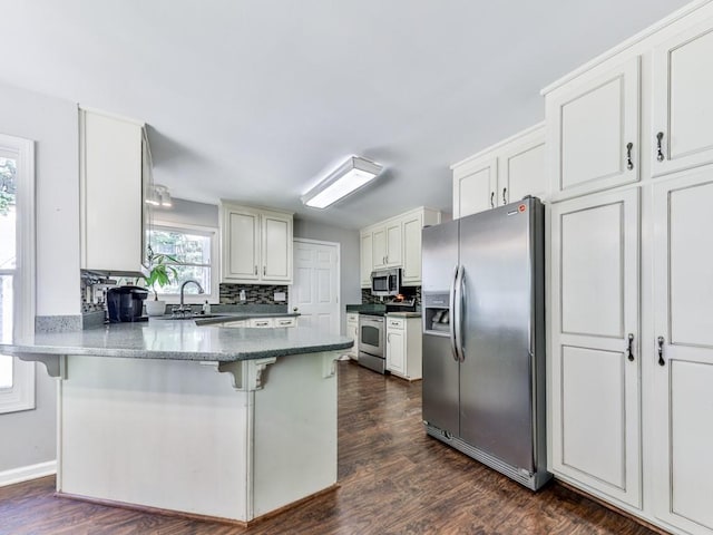 kitchen with stainless steel appliances, a sink, a peninsula, a kitchen breakfast bar, and backsplash