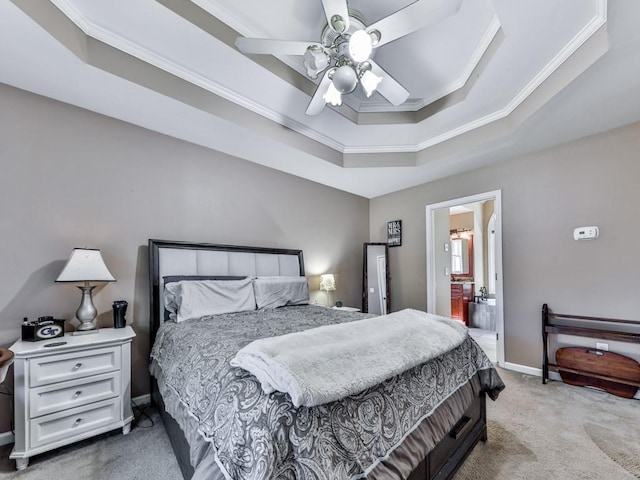 carpeted bedroom with a tray ceiling, crown molding, baseboards, ensuite bath, and a ceiling fan