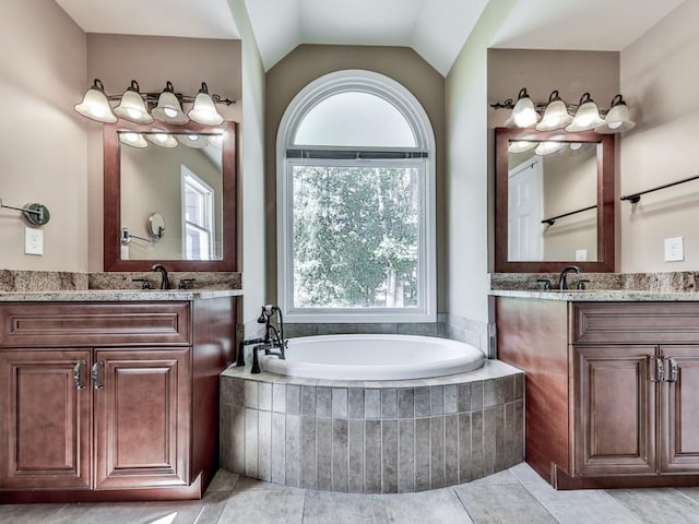 bathroom featuring two vanities, a bath, vaulted ceiling, and tile patterned floors