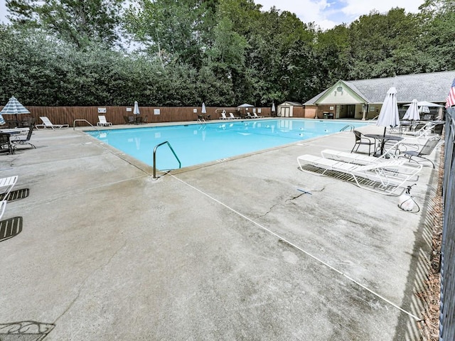 community pool with fence, a patio, and view of scattered trees