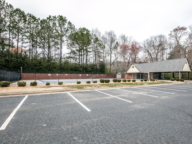 uncovered parking lot featuring fence and view of wooded area