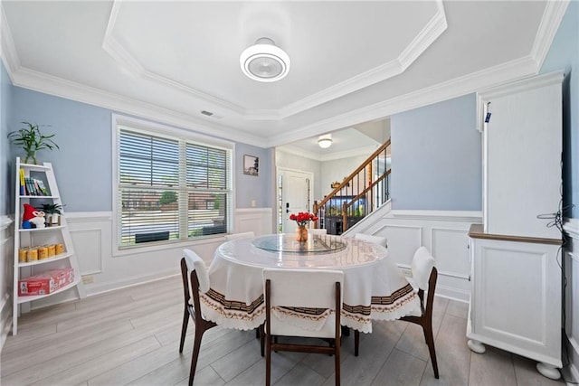 dining room featuring a decorative wall, stairway, light wood-style floors, and a tray ceiling