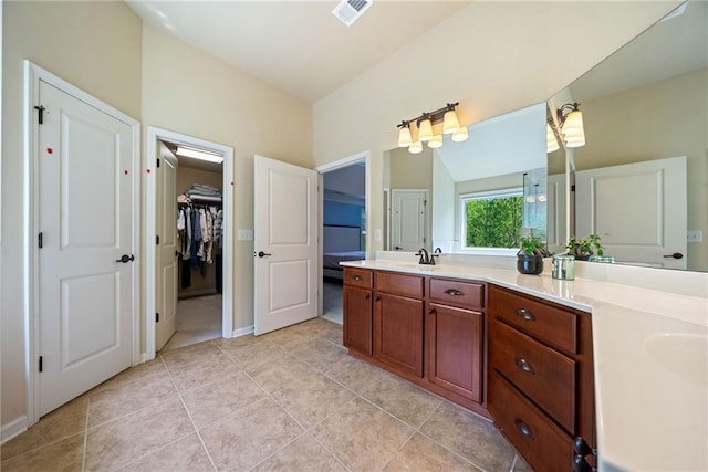 bathroom featuring visible vents, a sink, double vanity, a walk in closet, and tile patterned flooring