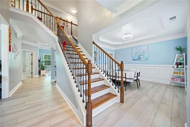 staircase featuring ornamental molding, wainscoting, visible vents, a decorative wall, and wood finished floors