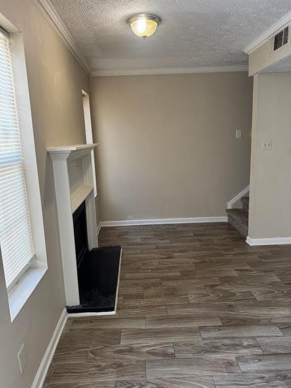unfurnished living room featuring crown molding, a fireplace with raised hearth, a textured ceiling, and visible vents