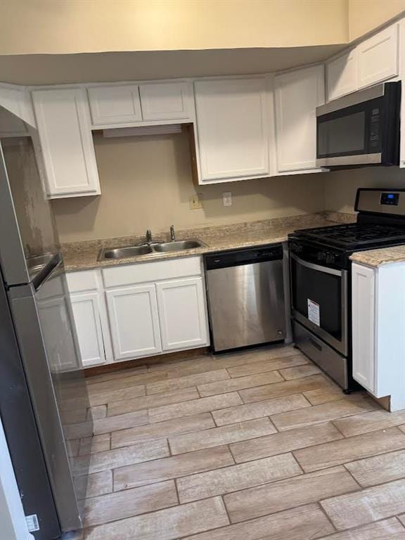 kitchen with light wood-type flooring, a sink, appliances with stainless steel finishes, and white cabinets
