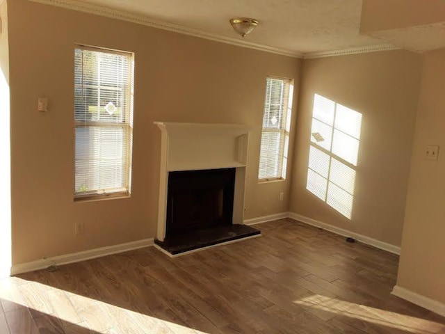 unfurnished living room with plenty of natural light, ornamental molding, a fireplace with raised hearth, and wood finished floors