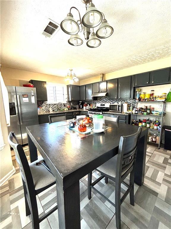 5687 Pine Meadow Ct, Morrow, GA 30260 - kitchen featuring appliances with stainless steel finishes, a textured ceiling, under cabinet range hood, visible vents, and an inviting chandelier