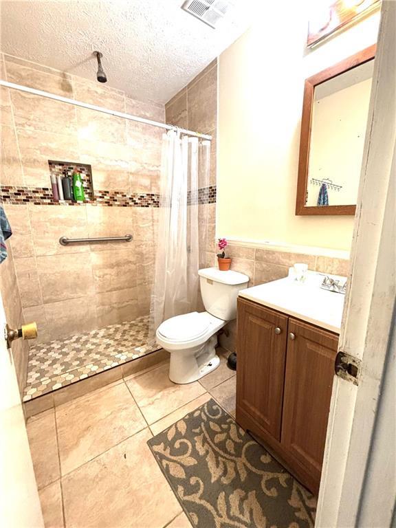 5687 Pine Meadow Ct, Morrow, GA 30260 - full bath with tile walls, toilet, a textured ceiling, visible vents, and tiled shower