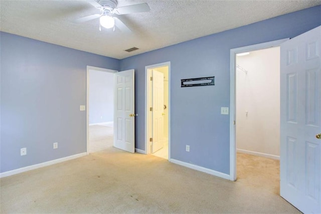 unfurnished bedroom with carpet flooring, a walk in closet, a textured ceiling, baseboards, and visible vents
