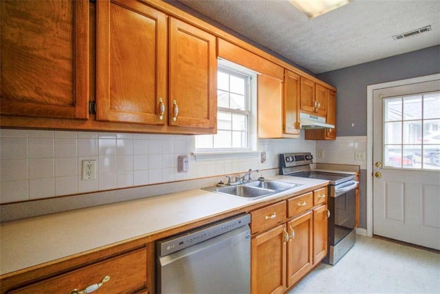kitchen featuring visible vents, brown cabinetry, under cabinet range hood, a sink, and appliances with stainless steel finishes