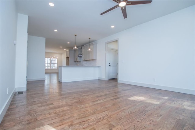 unfurnished living room featuring light wood-style floors, recessed lighting, baseboards, and ceiling fan with notable chandelier