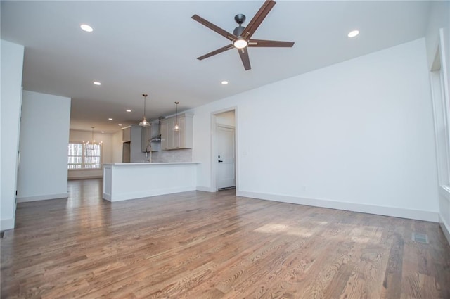 unfurnished living room with recessed lighting, light wood-style flooring, baseboards, and ceiling fan with notable chandelier